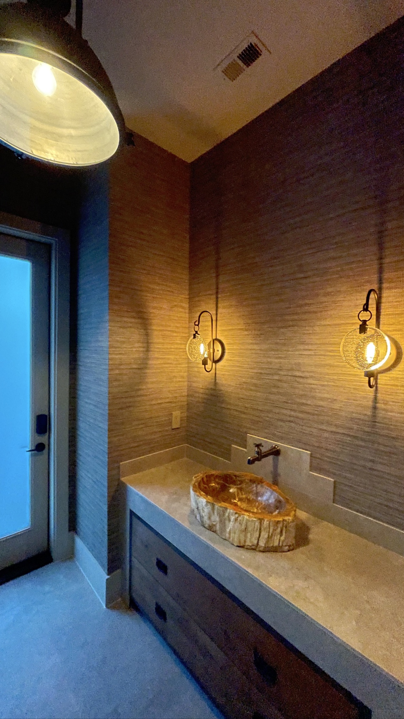 Warm textured grasscloth installed around a finished vanity with mirror and stone vessel sink