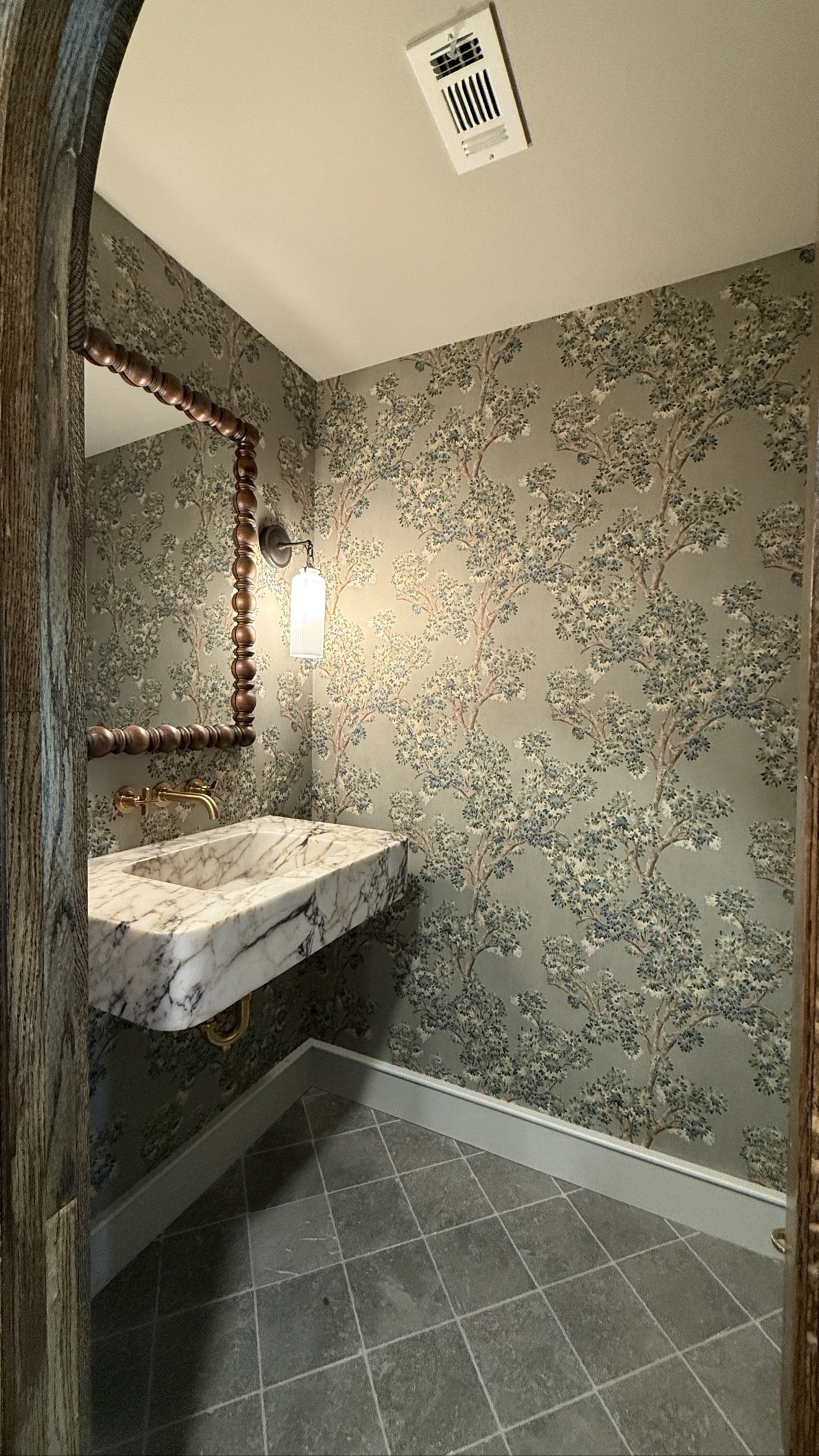 Tree-patterned wallpaper installed around a marble sink in a powder room