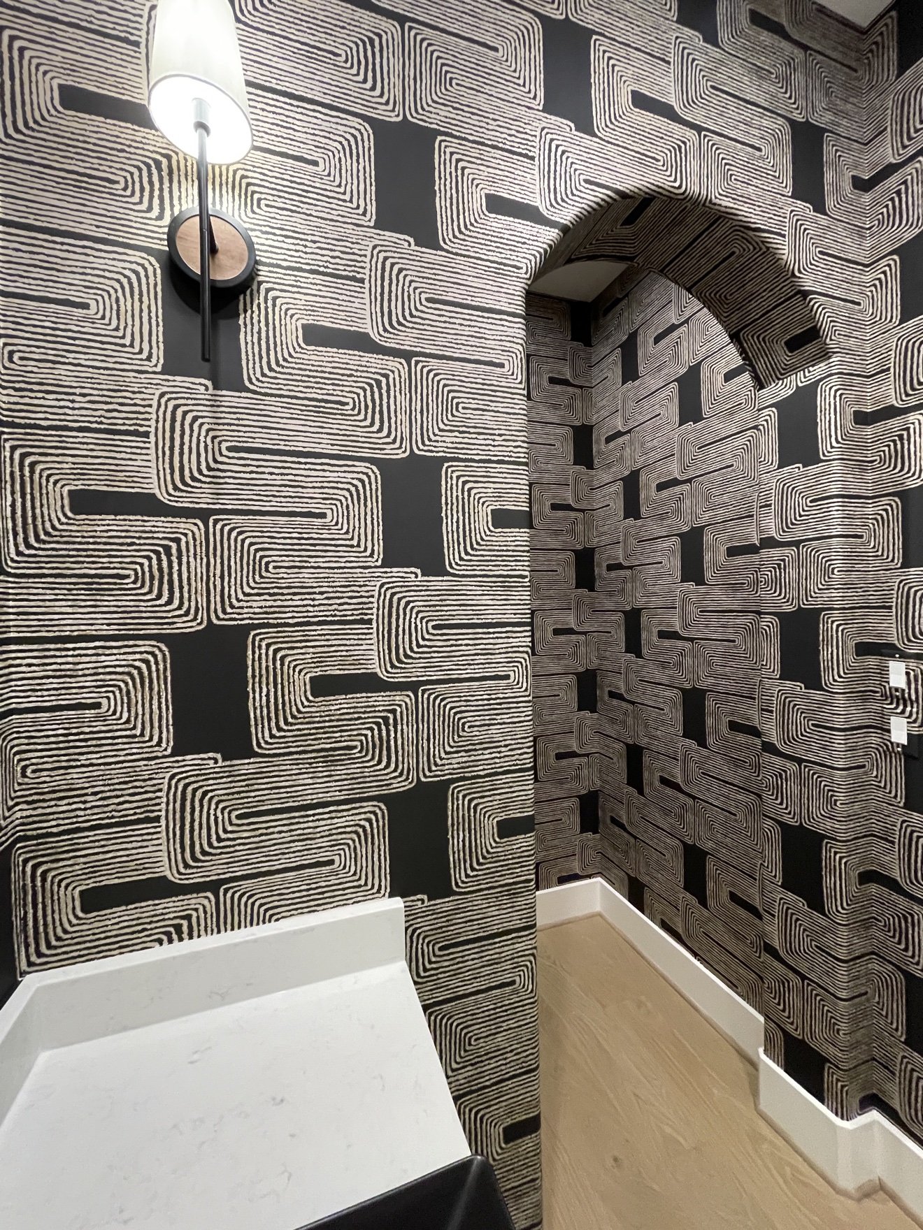 Black and cream geometric wallpaper installed throughout an arched powder room