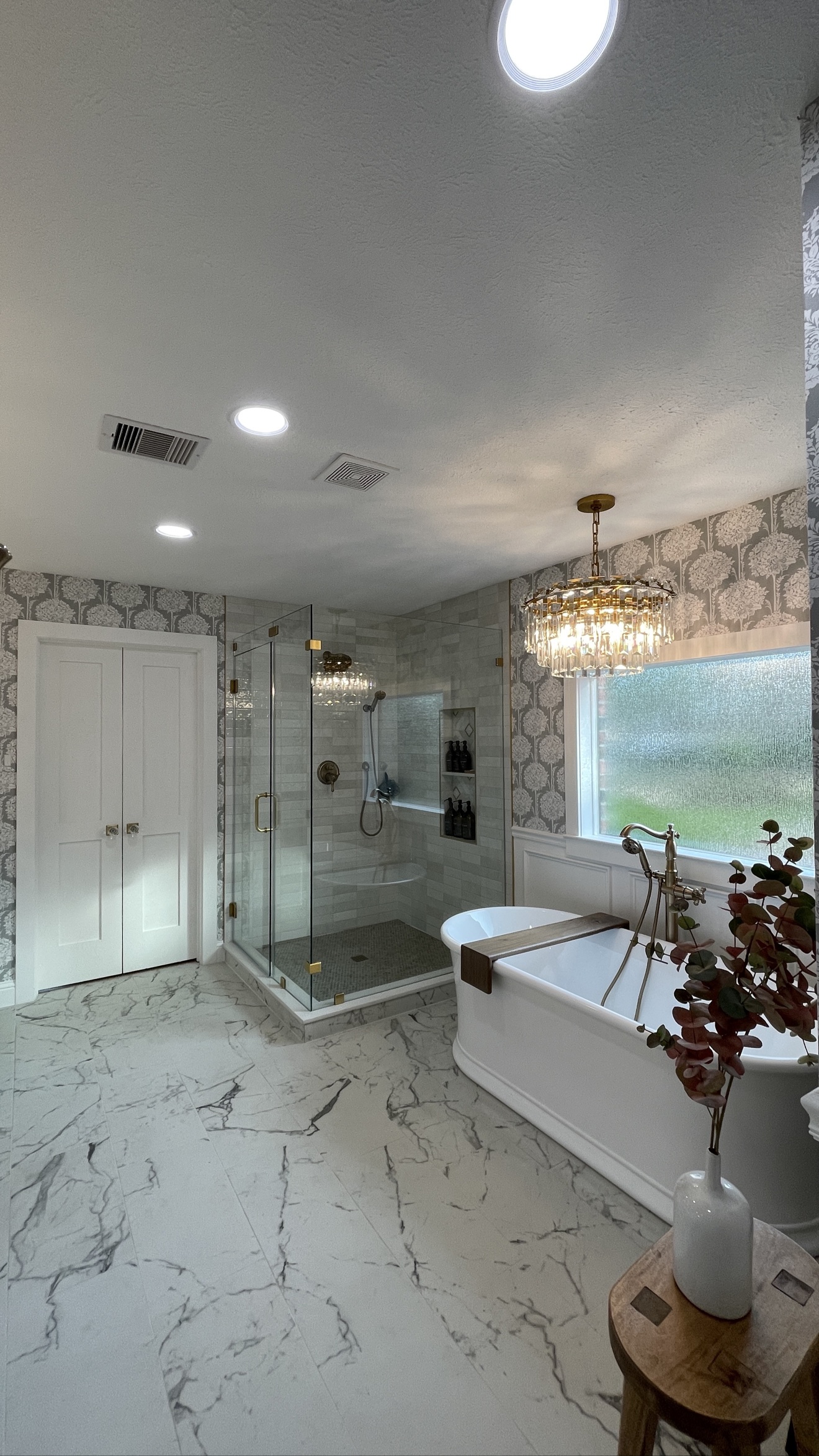 Gray floral wallpaper installed throughout a spacious primary bathroom