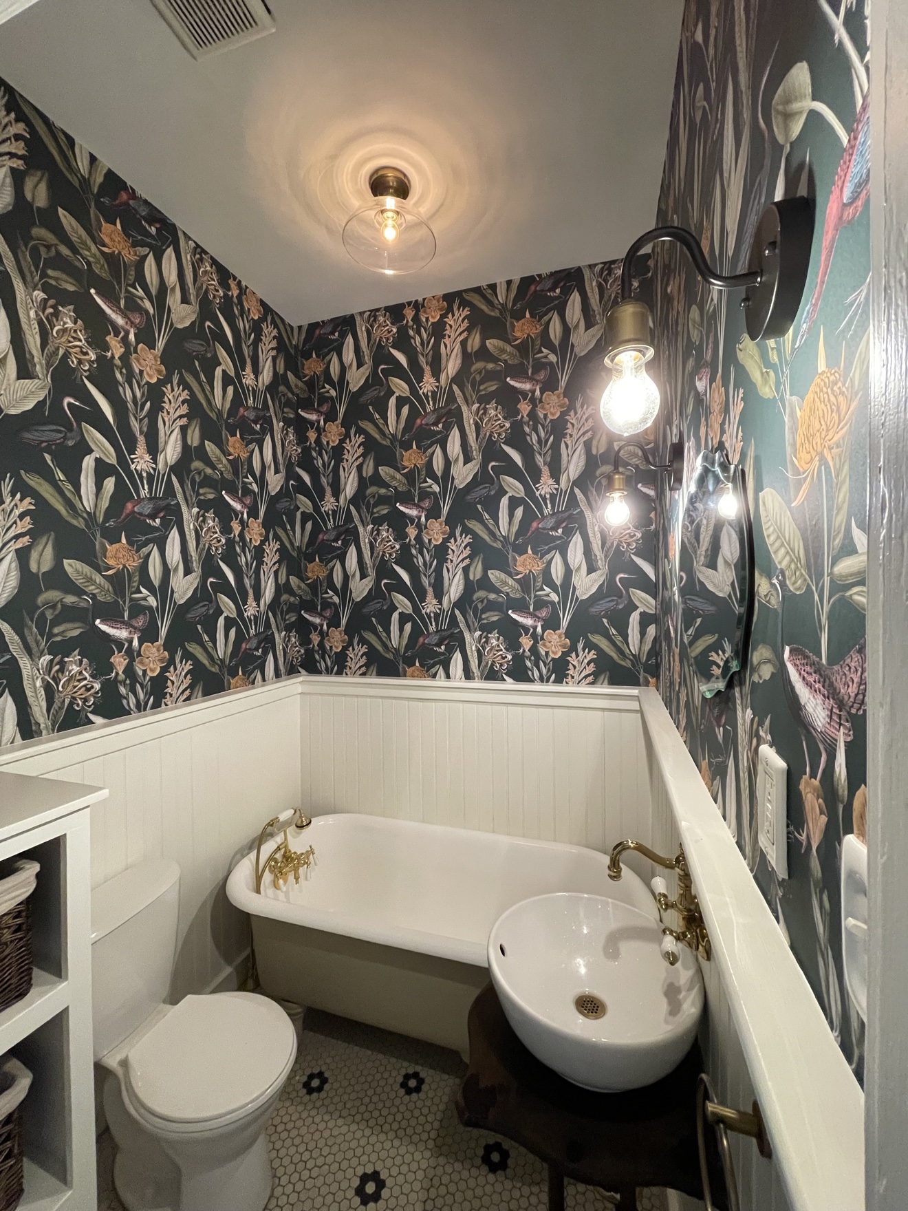 Dark botanical wallpaper installed above white bathroom paneling