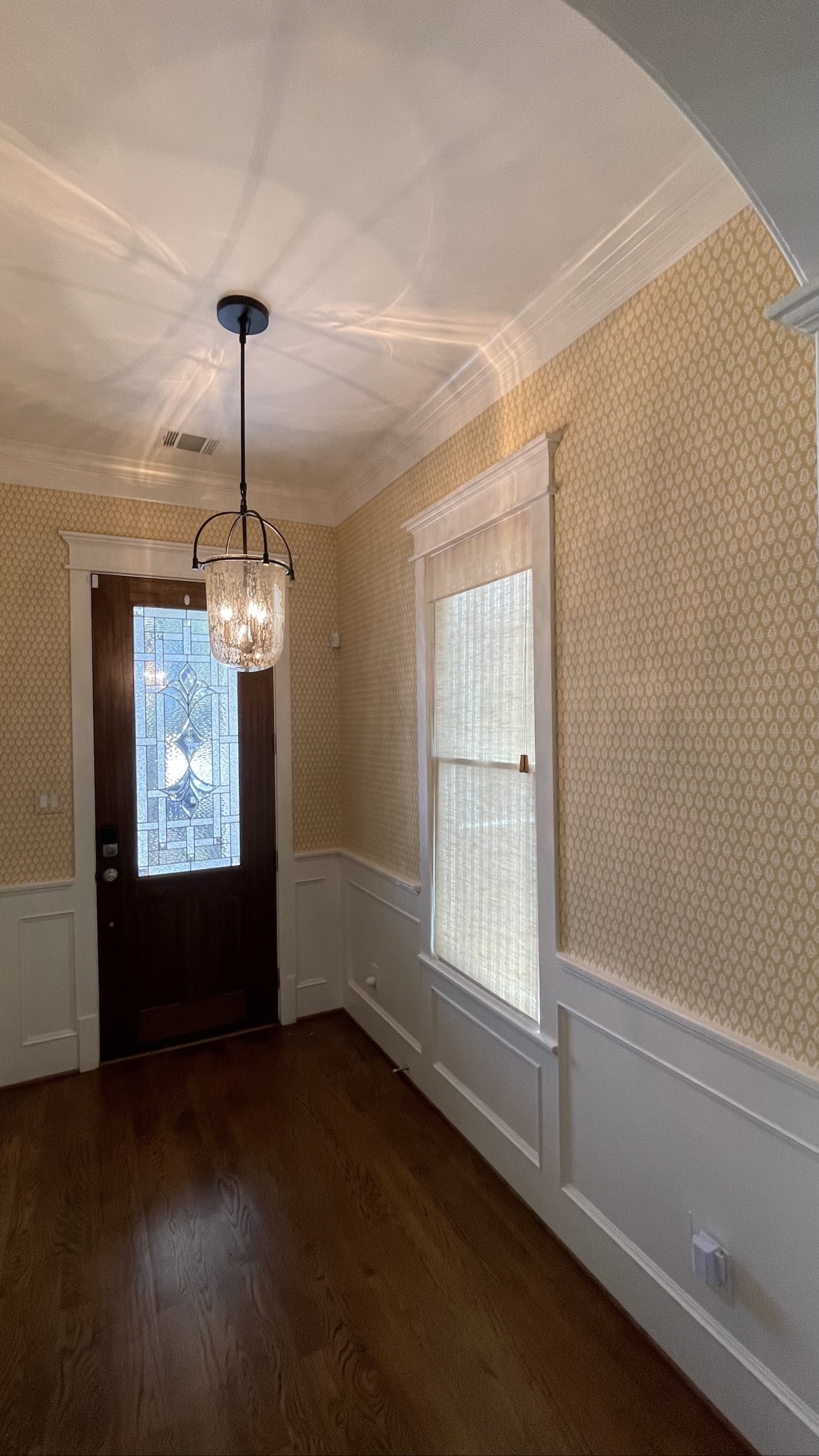 Gold patterned wallpaper installed above white paneling in a finished entry hall