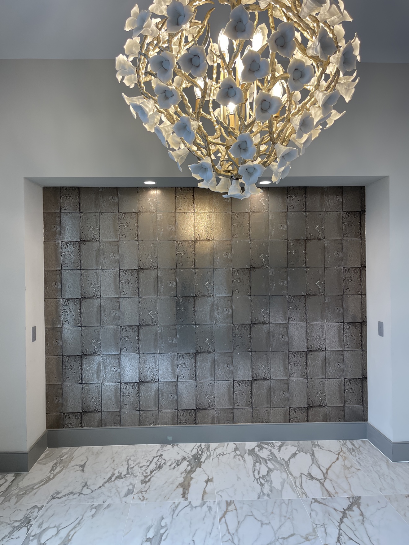 Metallic tile-pattern wallcovering installed beneath a floral statement chandelier