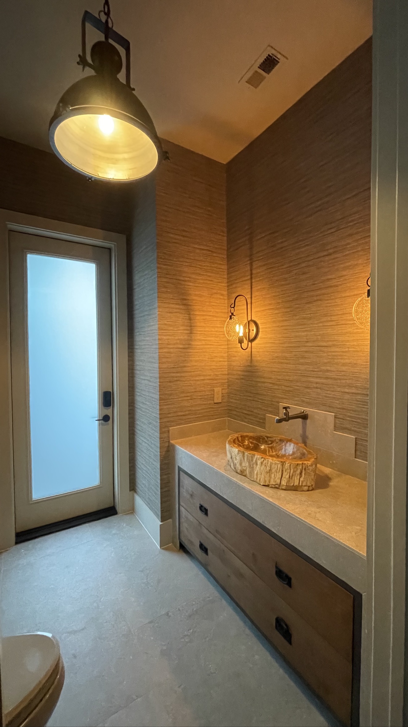 Warm grasscloth installed throughout a powder room with a stone vessel sink