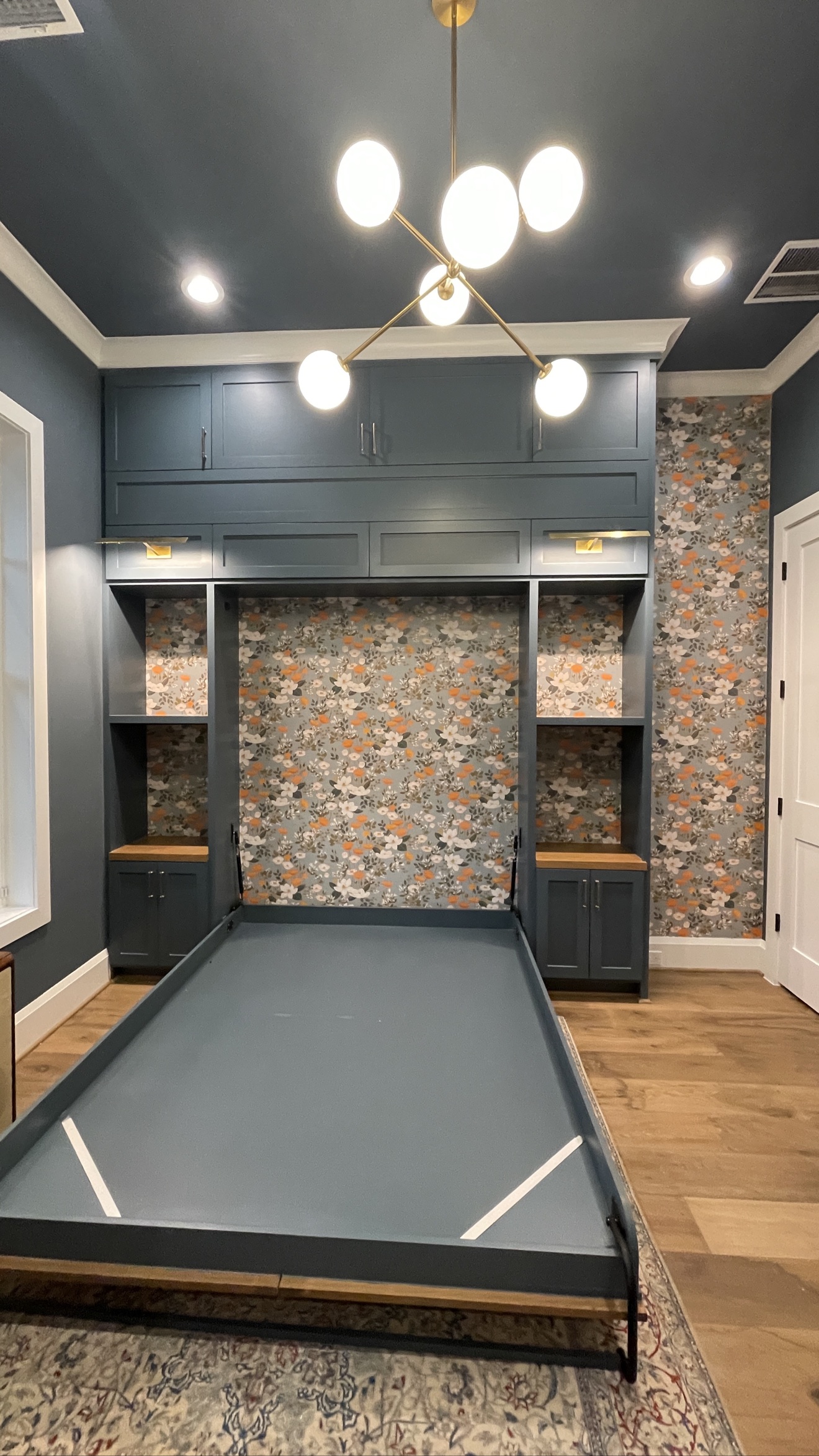 Floral wallpaper installed inside and beside custom built-ins with a concealed wall bed